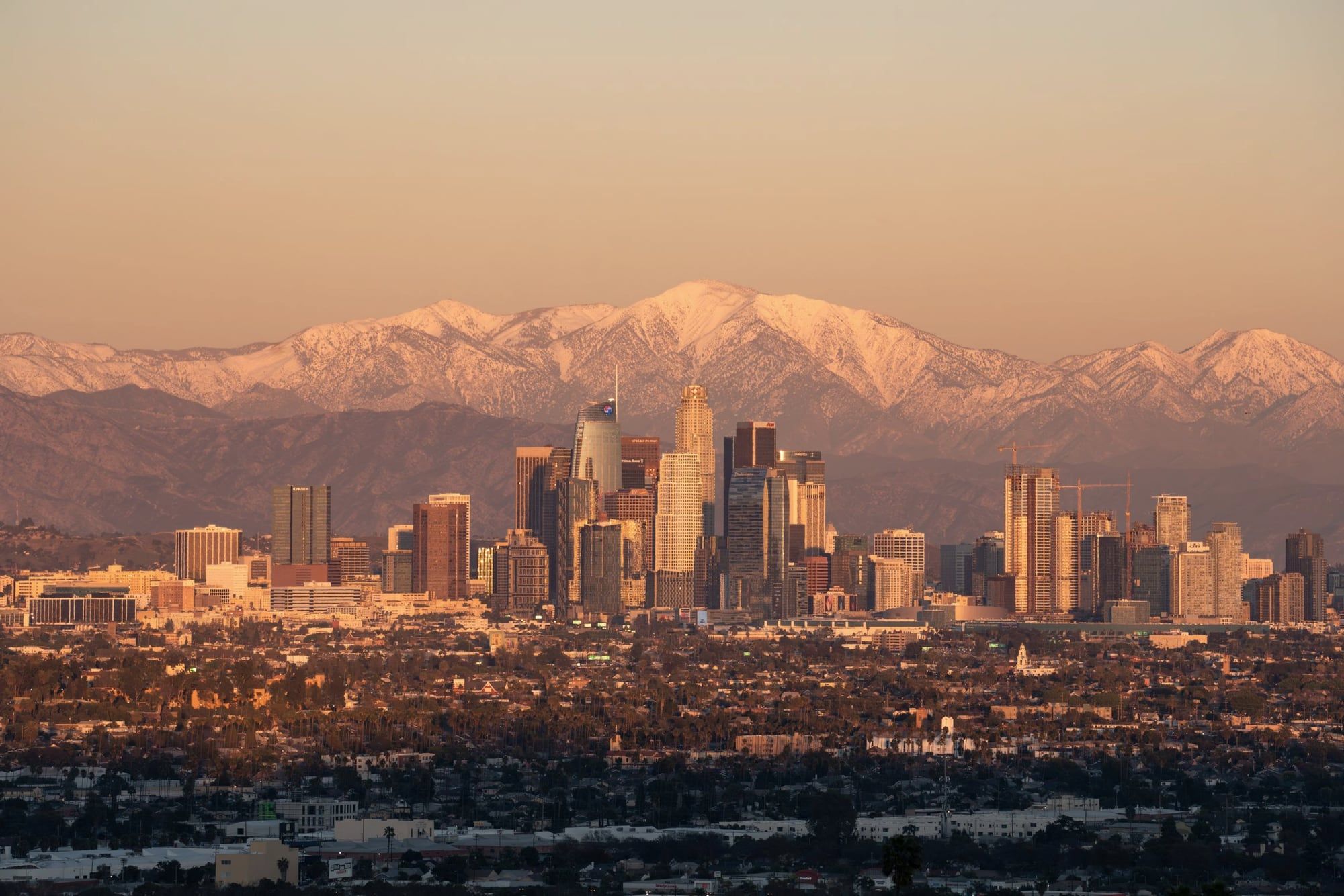 Downtown Los Angeles skyline at golden hour with snow covered mountains behind it